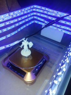 freshly resin-printed miniature curing under UV light — the final step before cleanup and paint.