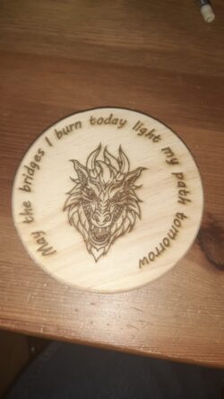 A laser-engraved wooden coaster featuring a detailed dragon and a quote that every tabletop adventurer will appreciate.